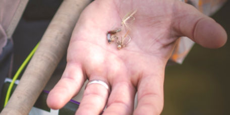 An angler holds a few dry flies in the palm of their hand.